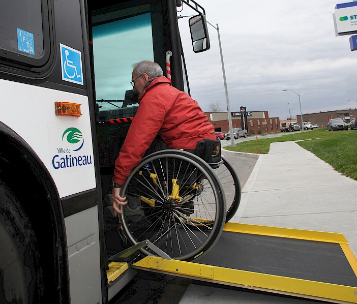 Photo d’une personne en fauteuil roulant montant à bord d'un autobus munis d'une rampe d'accès.